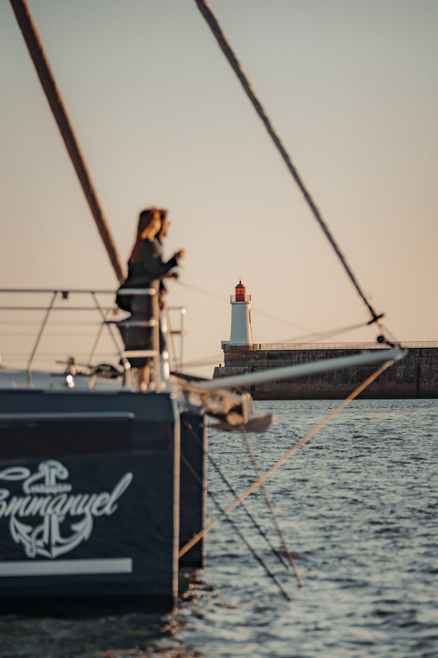Sailboat near a lighthouse during sunset, woman on deck enjoying the view.