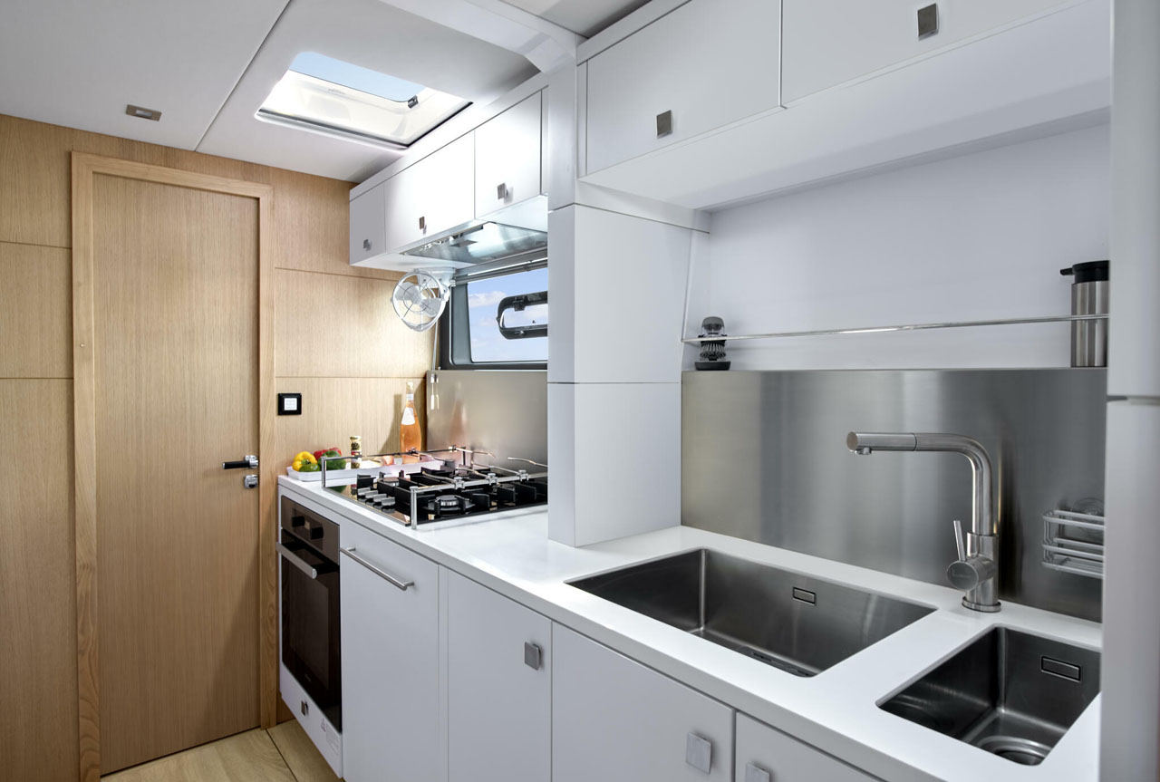 Modern yacht kitchen with stainless steel appliances, dual sinks, and wooden accents.