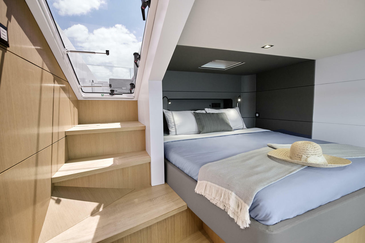 Luxurious yacht bedroom with modern design, wooden steps, skylight, cozy bed, and straw hat on a blanket.