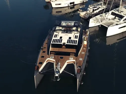 Aerial view of a sleek, modern catamaran docked in a marina, surrounded by other boats under a clear sky.