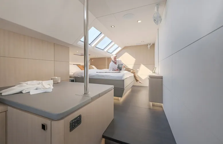 Spacious, modern yacht bedroom with skylights and a person reading on the bed, featuring sleek, minimalist design.