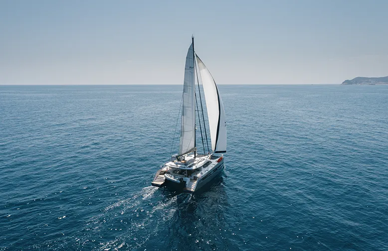 Sailing catamaran gliding through calm blue sea under clear sky, perfect for ocean travel and leisure exploration.