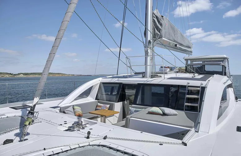 Luxurious catamaran sailing on open water under a clear blue sky, featuring a spacious deck with seating and a table.
